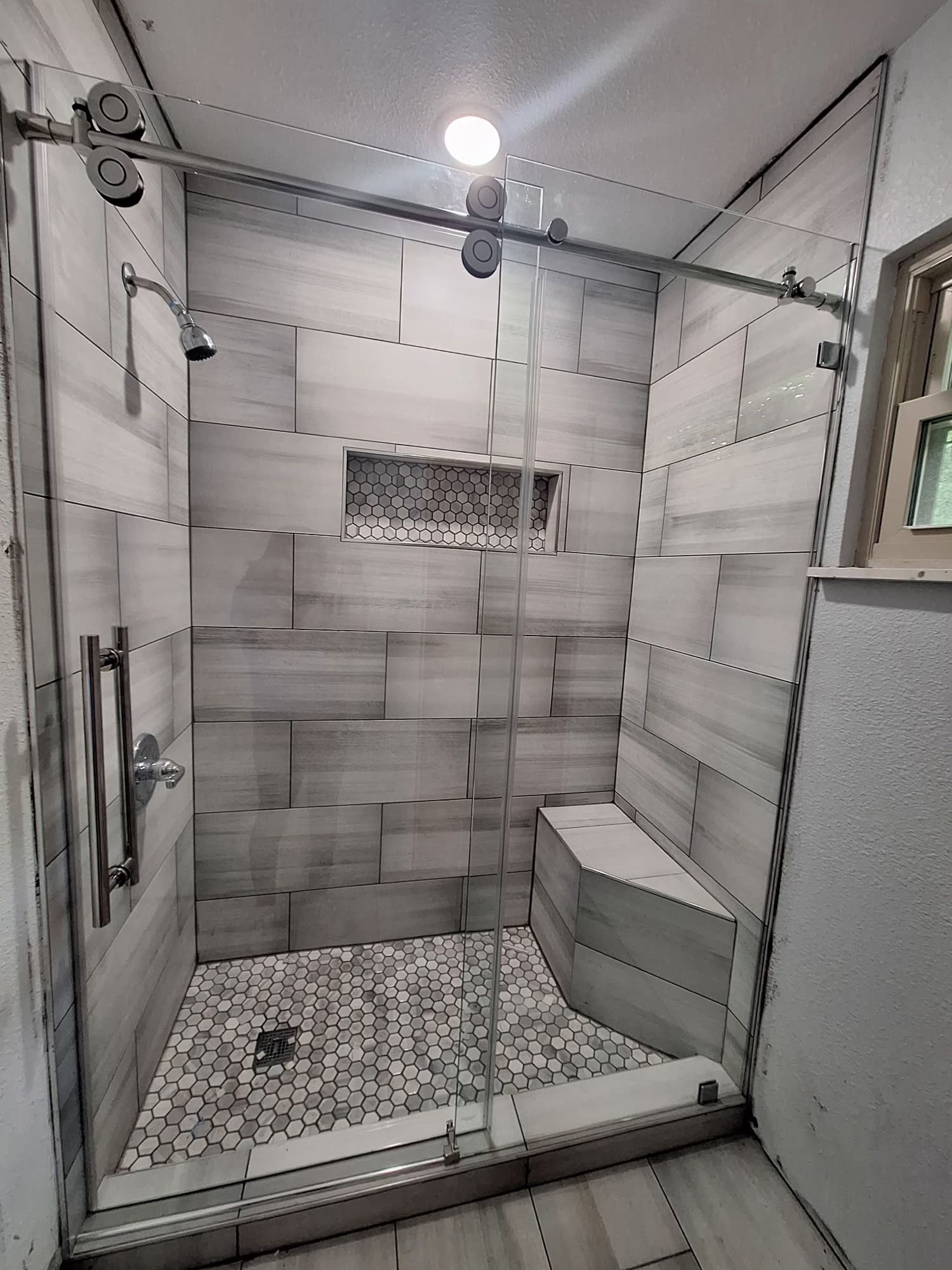 Walk-in shower with gray stone tile, bench and glass enclosure