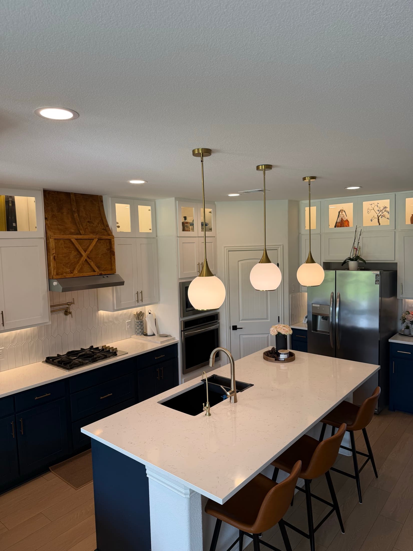 Custom kitchen with navy cabinetry, wood hood and gold lighting